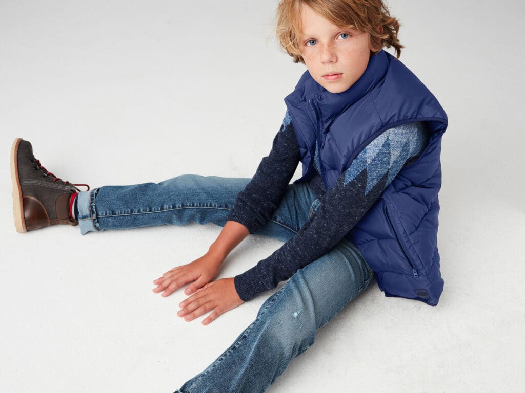 Young boy in blue puffer jacket and jeans sitting