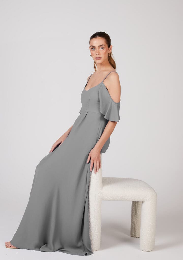 Woman in elegant gray dress posing beside modern chair